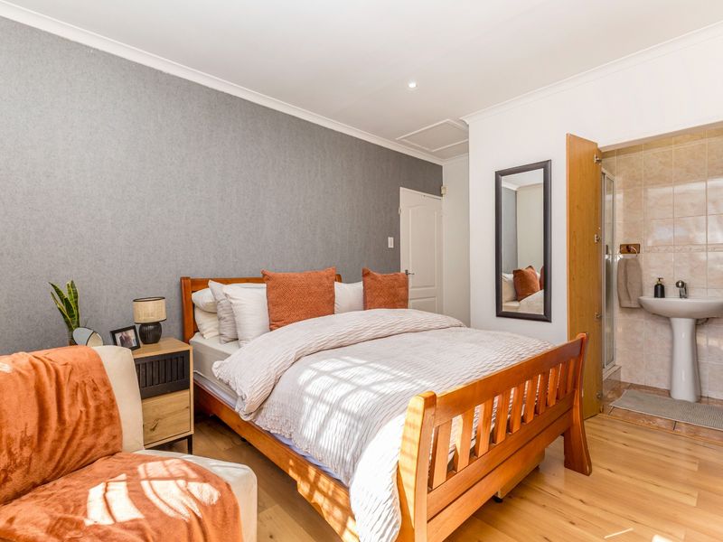 A well-maintained bedroom featuring laminate flooring, a feature wall, and an attached en-suite bathroom with a pedestal basin and shower enclosure.