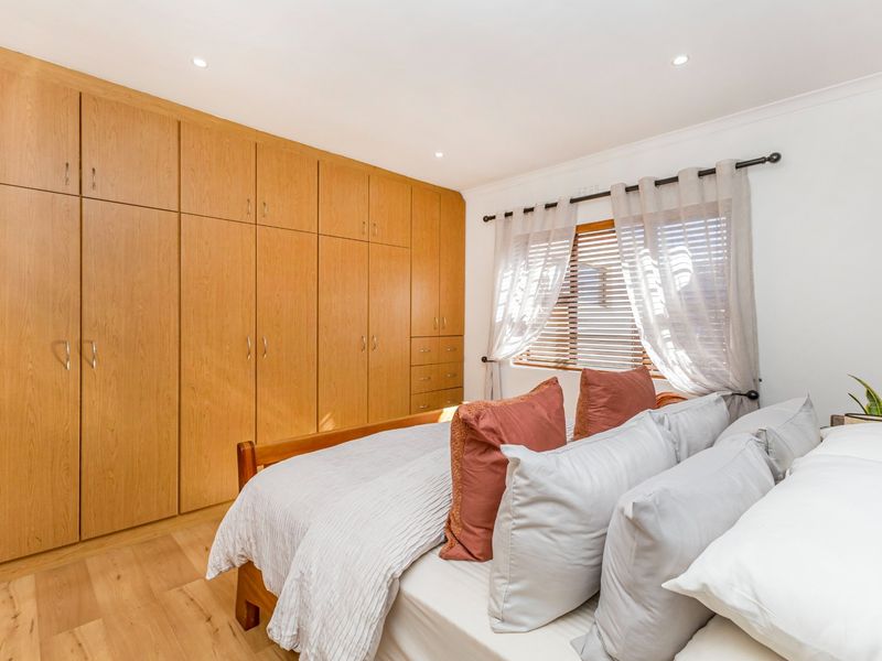 A well-maintained bedroom featuring extensive floor-to-ceiling built-in wooden cabinetry, light timber flooring, and natural light through venetian blinds.