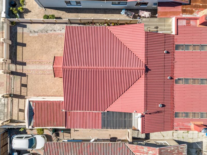 Aerial view of the property showing the corrugated metal roof, paved driveway, and surrounding boundary walls.