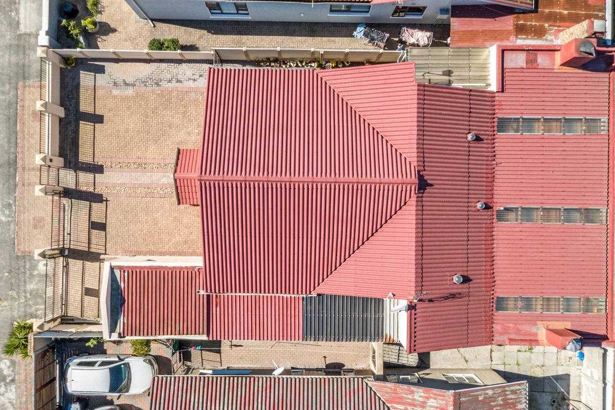 Aerial view of the property showing the corrugated metal roof, paved driveway, and surrounding boundary walls.