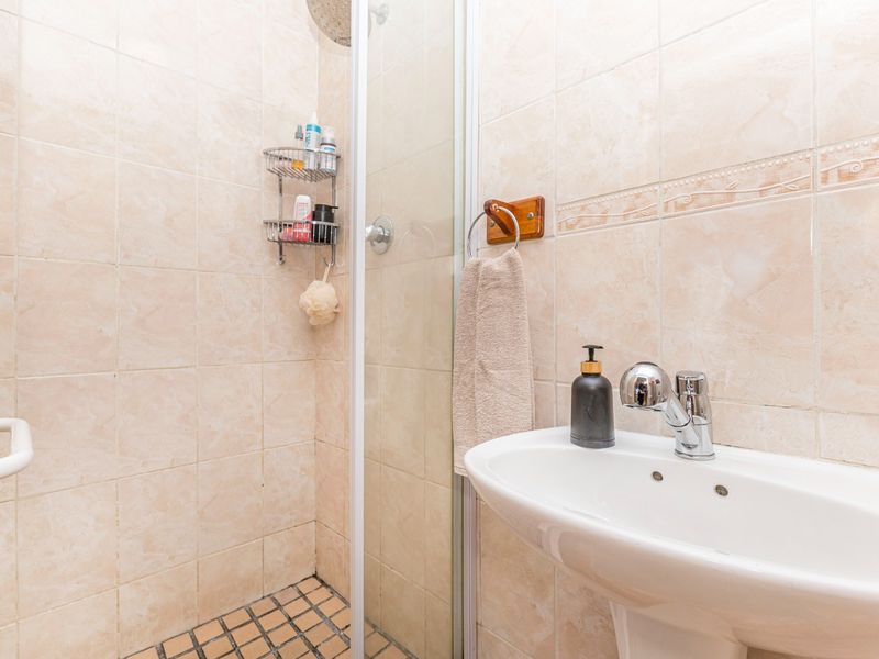 A functional bathroom featuring a pedestal basin with chrome mixer tap and a tiled shower enclosure with glass door.