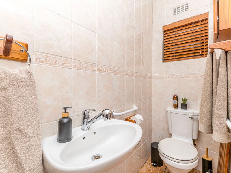 A compact bathroom featuring neutral ceramic wall and floor tiles, a pedestal washbasin with chrome mixer tap, and a standard toilet.