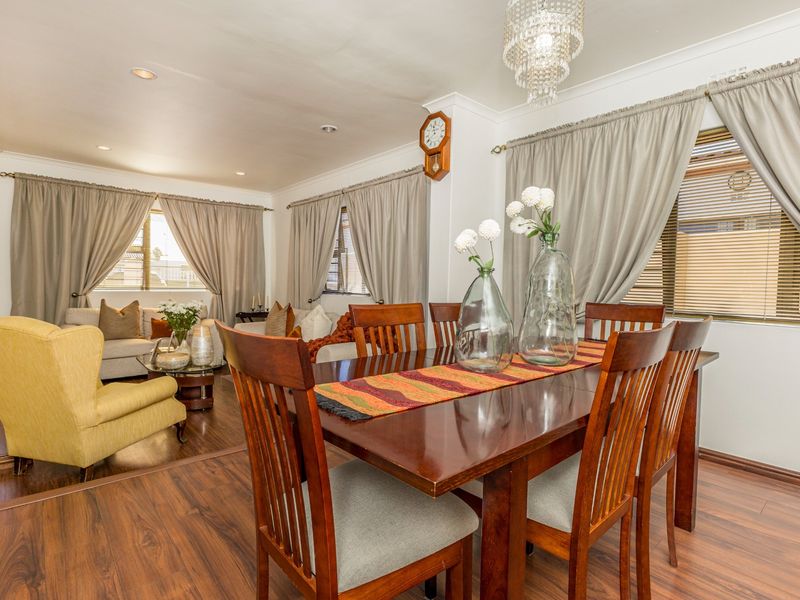 An open-plan living and dining area featuring dark laminate flooring, recessed lighting, and a decorative crystal chandelier.
