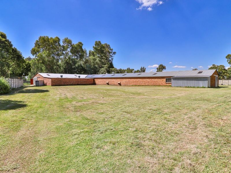 Rear view of a large industrial brick building with a corrugated metal roof, set on a spacious grass lot with perimeter boundary walling.