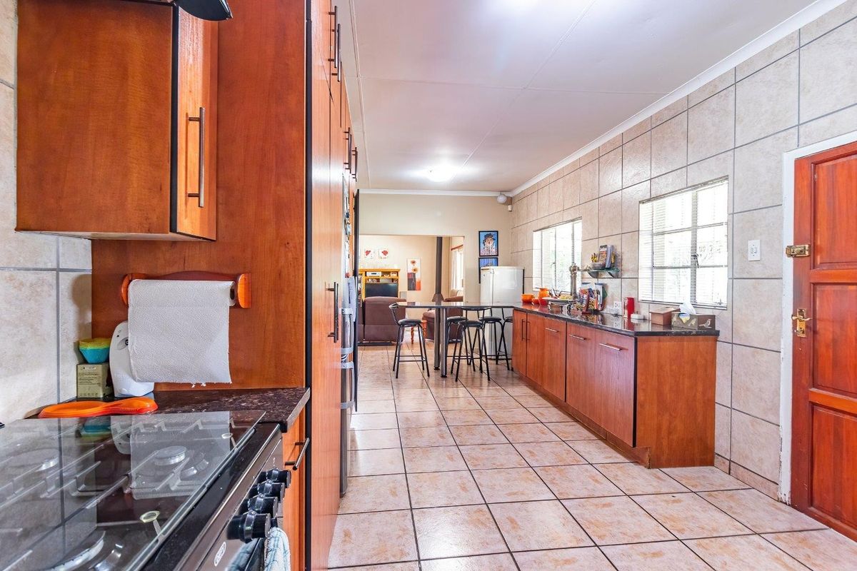 Spacious kitchen featuring wooden cabinetry, granite countertops, gas hob, and tiled flooring, with an open-plan layout leading into the living area.