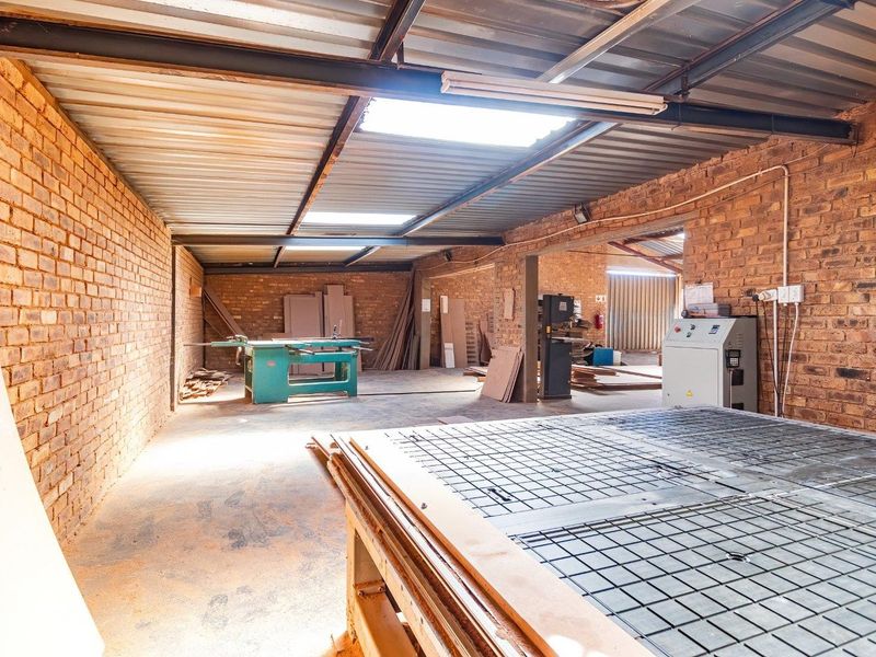 Spacious industrial workshop area featuring exposed brick walls, high corrugated metal ceilings with skylights, and durable concrete flooring suitable for manufacturing or storage.