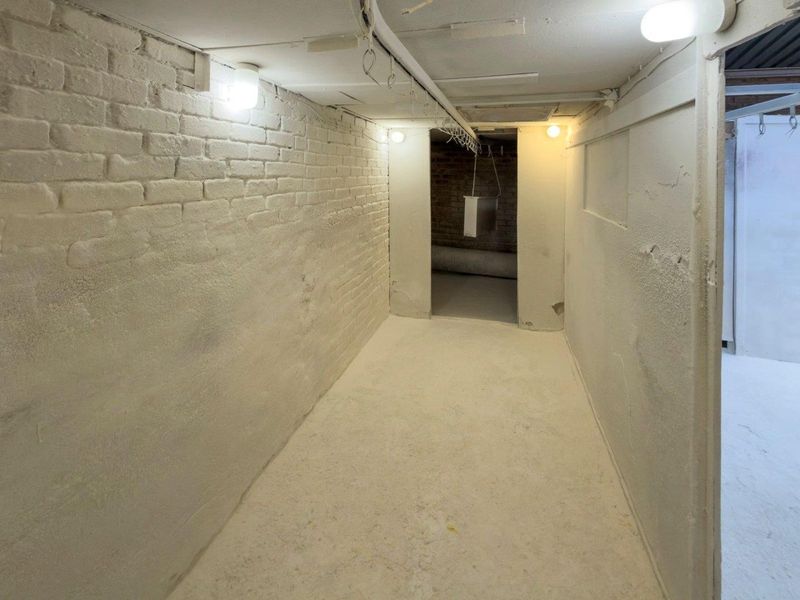 A functional utility or storage space featuring painted brick walls, overhead lighting, and a ceiling-mounted hanging rail system.