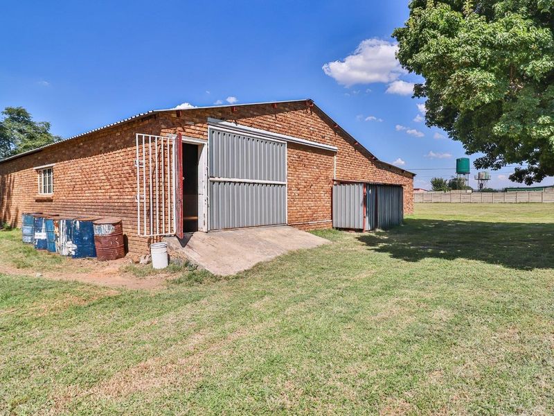 Rear view of an industrial brick building featuring a large sliding metal door, concrete access ramp, and an attached metal storage unit.