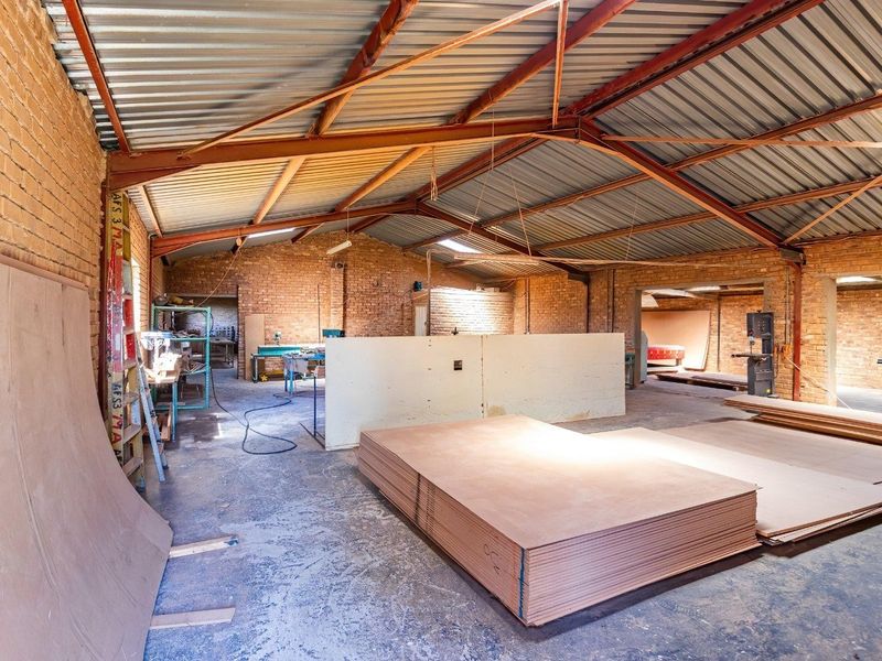 Spacious industrial utility area featuring exposed brick walls, a high steel truss roof with corrugated metal sheeting, and durable concrete flooring.
