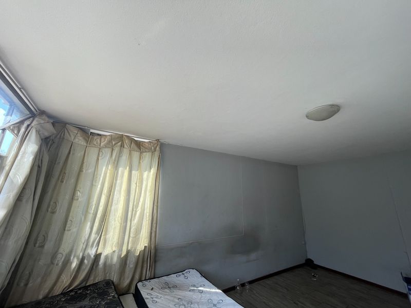 A bedroom featuring laminate flooring and a ceiling light fixture, currently showing signs of wall staining and requiring cosmetic attention.