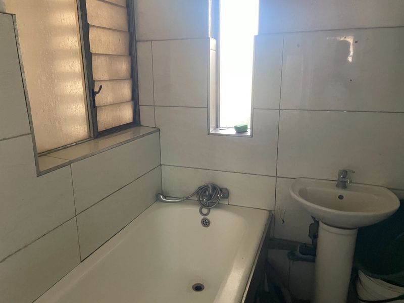 A dated bathroom featuring a standard bathtub, pedestal basin, and tiled walls, requiring modernization to improve its overall condition and aesthetic appeal.
