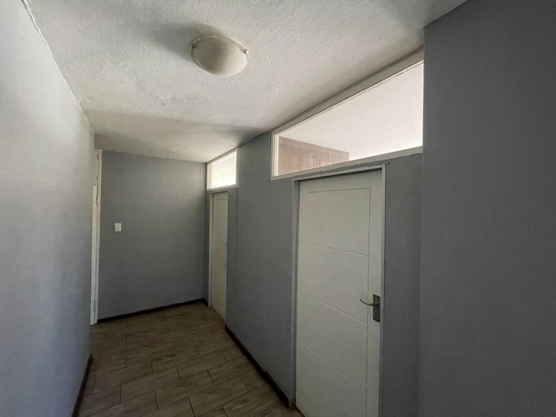 A vacant hallway featuring tiled flooring, neutral grey walls, and transom windows above the interior doors, providing a clean and functional transition space.