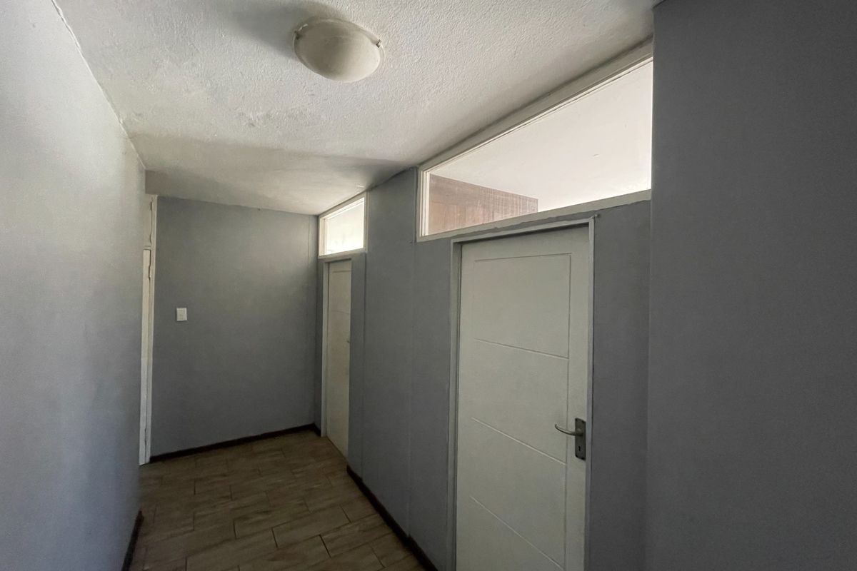 A vacant hallway featuring tiled flooring, neutral grey walls, and transom windows above the interior doors, providing a clean and functional transition space.