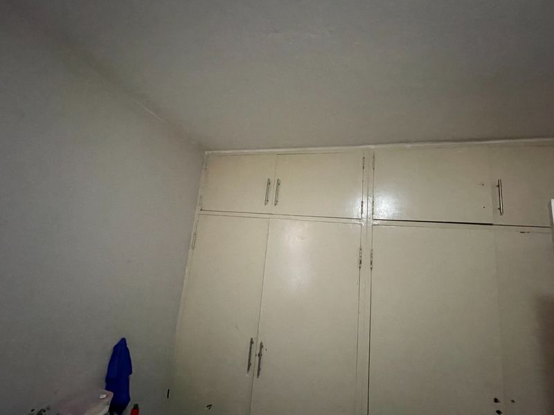 A bedroom featuring floor-to-ceiling built-in cupboards with a dated finish, offering ample storage space.