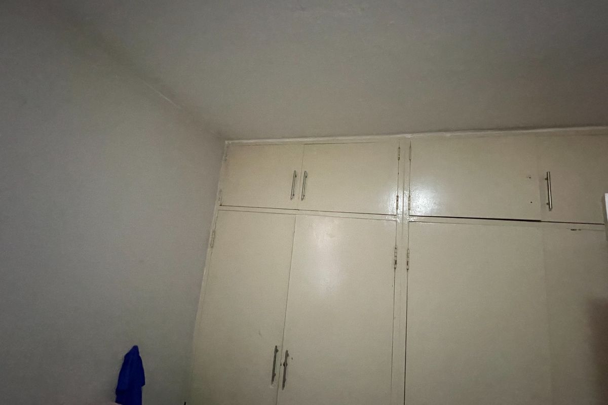 A bedroom featuring floor-to-ceiling built-in cupboards with a dated finish, offering ample storage space.