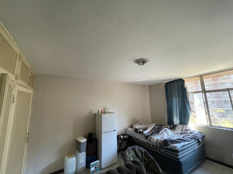 A bedroom featuring built-in cupboards and tiled flooring, offering a functional space with potential for cosmetic updates.