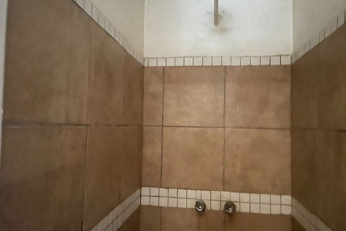 A shower enclosure featuring brown wall tiles with decorative mosaic borders, a fixed shower head, and wall-mounted mixer controls.