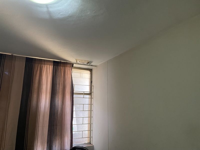 A bedroom interior featuring a window with security bars and visible ceiling damage near the window frame.