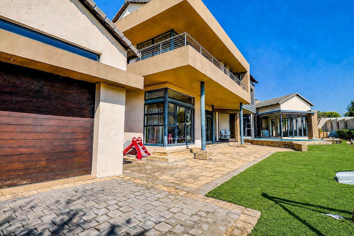 Spacious rear exterior featuring a paved patio, balcony, swimming pool, and well-maintained lawn, providing an ideal setting for outdoor living and entertainment.