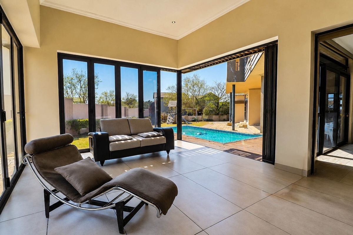 Bright living area featuring large bi-fold glass doors that open directly onto a wooden deck and swimming pool area.