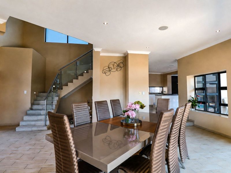 Spacious open-plan dining area featuring tiled flooring, recessed lighting, and a modern staircase with a glass balustrade, flowing into the kitchen area.
