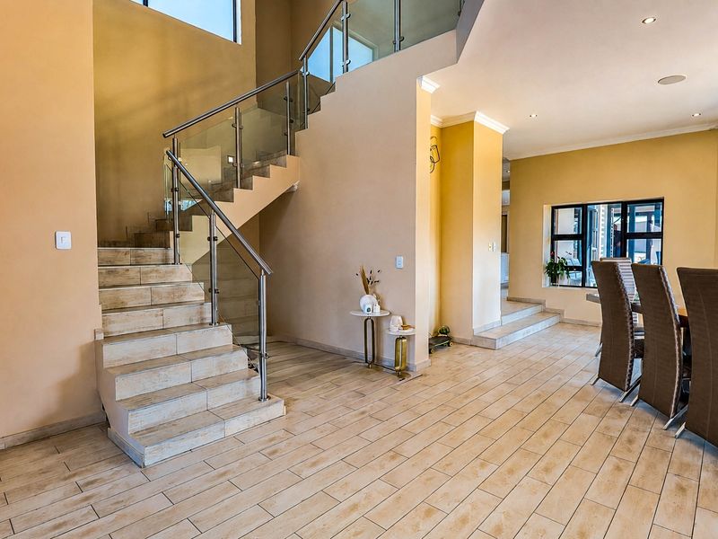 Spacious open-plan living area featuring a modern staircase with glass balustrades, tiled flooring, and recessed lighting throughout.