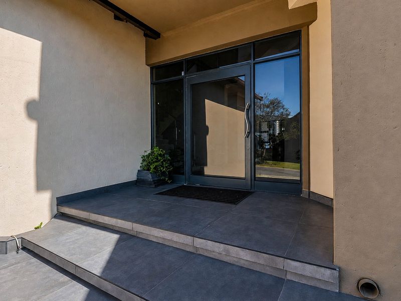 A modern entrance featuring a glass front door with sidelights and a clean, tiled porch area.