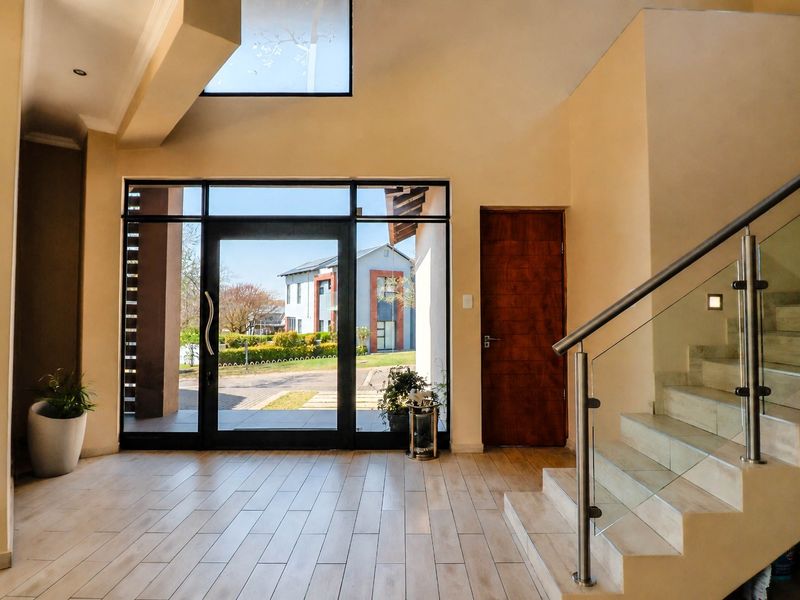 Spacious modern entrance hall featuring a glass balustrade staircase, tiled flooring, and a large glass door providing ample natural light.