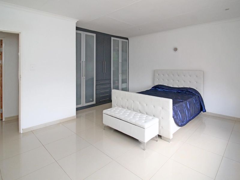 Spacious bedroom featuring neutral tiled flooring and modern built-in cupboards with glass panel detailing.