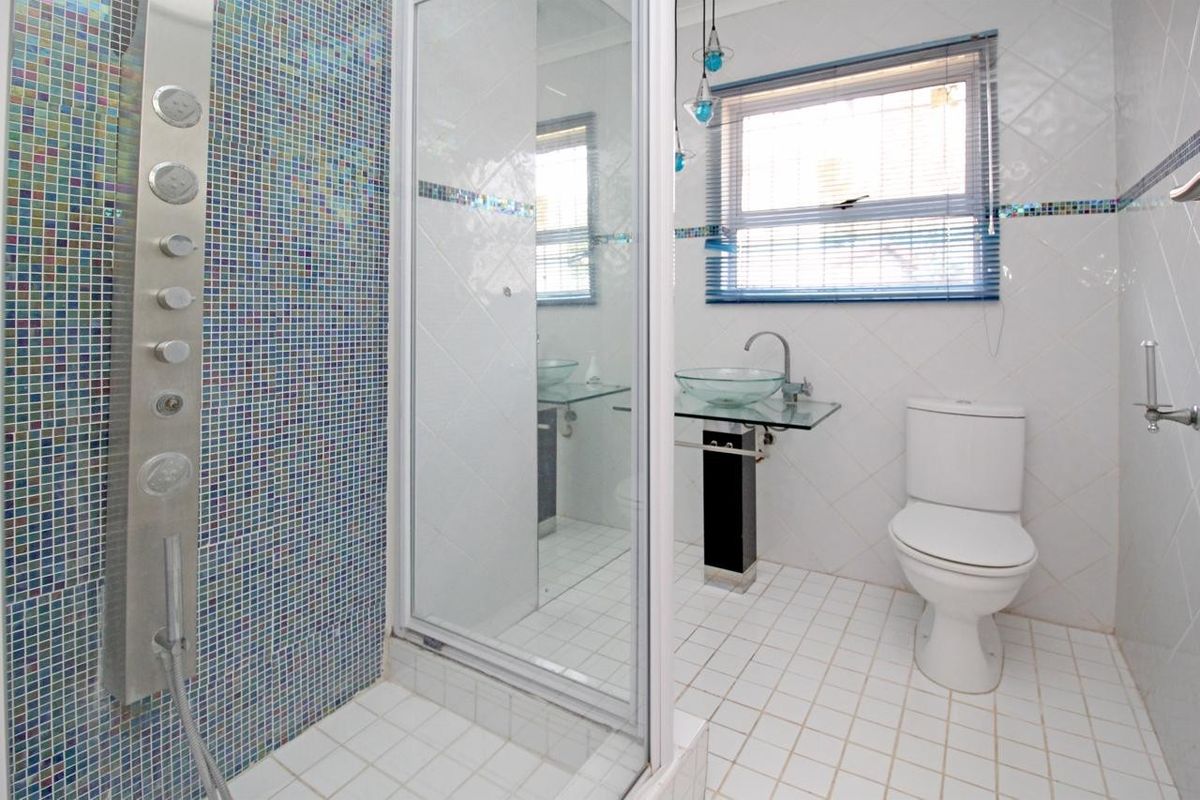A functional bathroom featuring a glass shower enclosure with a mosaic tile accent wall, pedestal basin, and standard toilet.