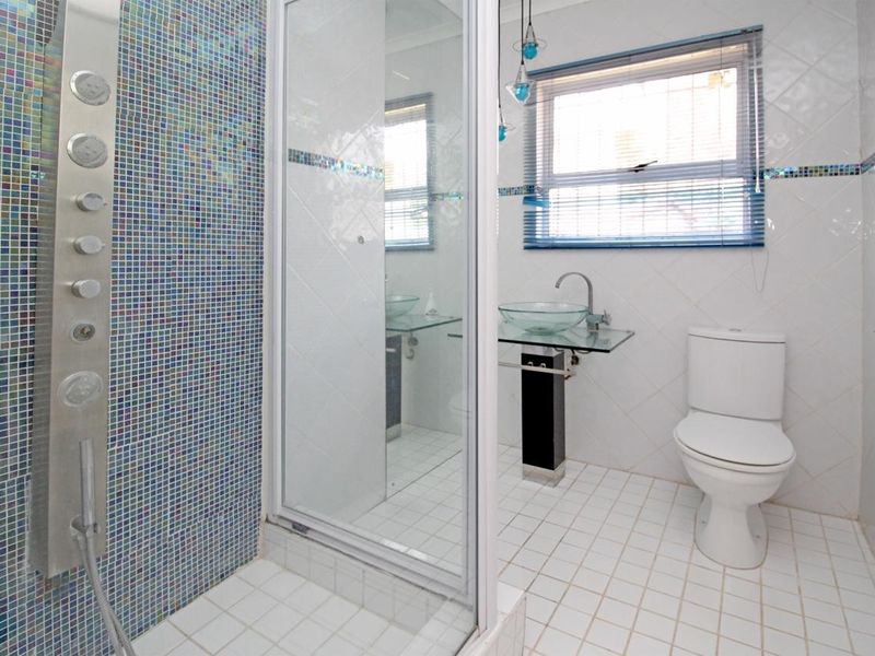 A functional bathroom featuring a glass shower enclosure with a mosaic tile accent wall, pedestal basin, and standard toilet.