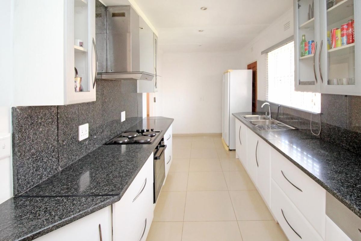 A functional galley-style kitchen featuring white cabinetry, dark granite countertops, a built-in oven, electric hob, and a double basin sink.