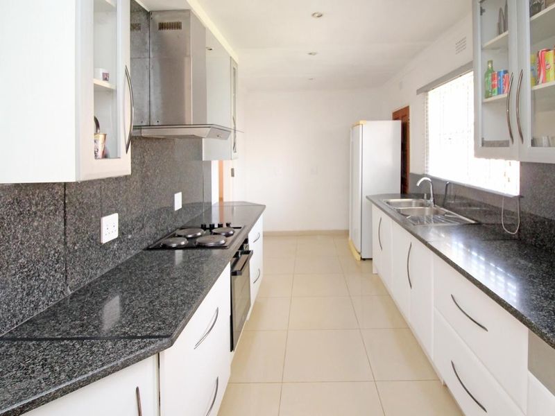 A functional galley-style kitchen featuring white cabinetry, dark granite countertops, a built-in oven, electric hob, and a double basin sink.