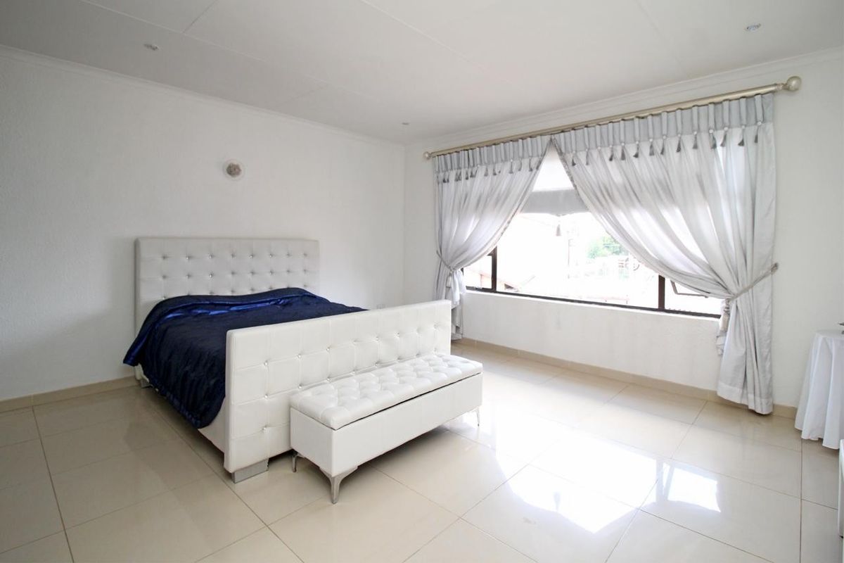 A bright and spacious bedroom featuring neutral tiled flooring, recessed ceiling lighting, and a large window allowing for ample natural light.