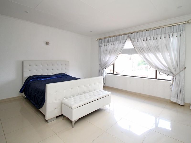 A bright and spacious bedroom featuring neutral tiled flooring, recessed ceiling lighting, and a large window allowing for ample natural light.