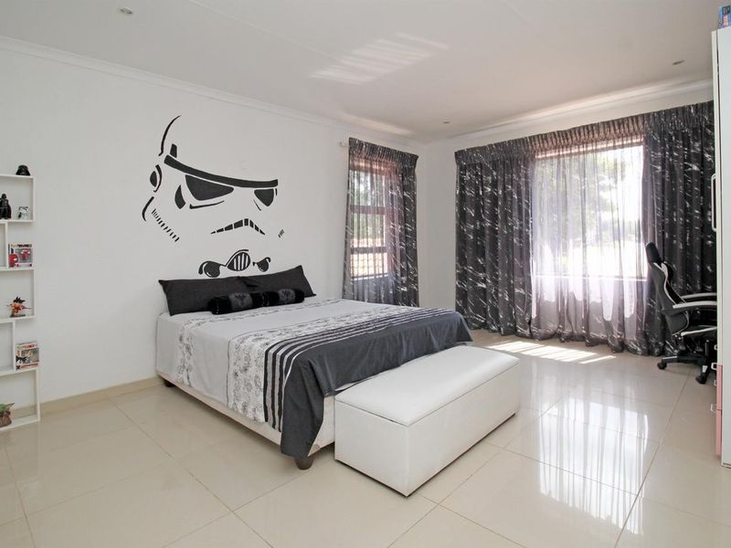 A spacious bedroom featuring neutral tiled flooring, recessed lighting, and large windows with curtain tracks, offering a clean and well-maintained living space.