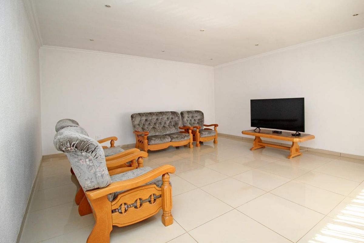 A spacious living room featuring neutral white walls, large format floor tiles, and recessed ceiling lighting.