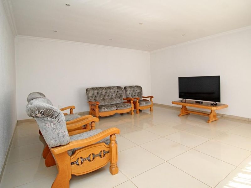 A spacious living room featuring neutral white walls, large format floor tiles, and recessed ceiling lighting.