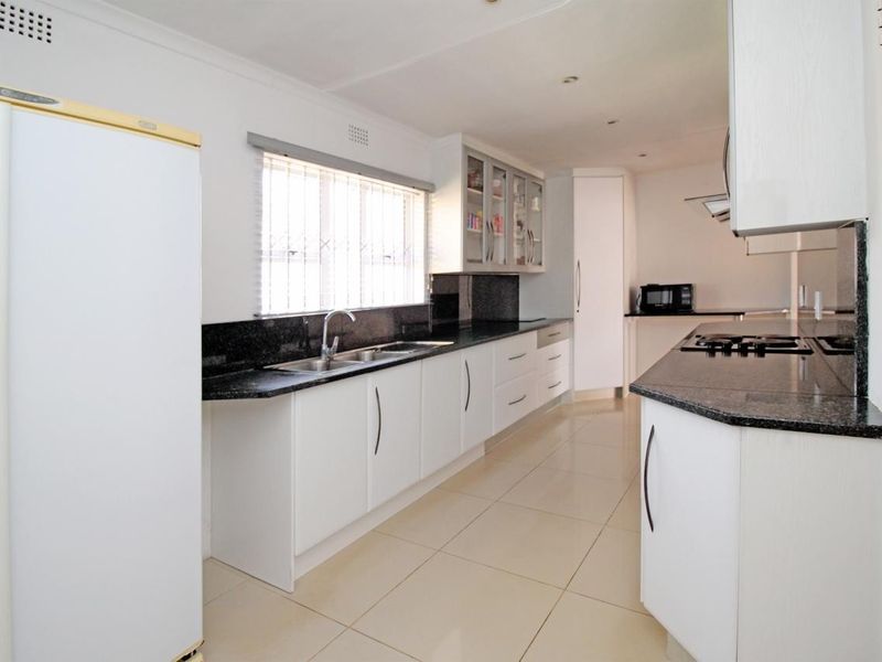 A clean, modern kitchen featuring white cabinetry, contrasting black granite countertops, a double bowl sink, and integrated gas hob with extractor fan.