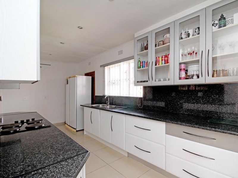 Modern kitchen featuring granite countertops, ample built-in cabinetry with glass-front upper units, a stainless steel sink, and a built-in hob.