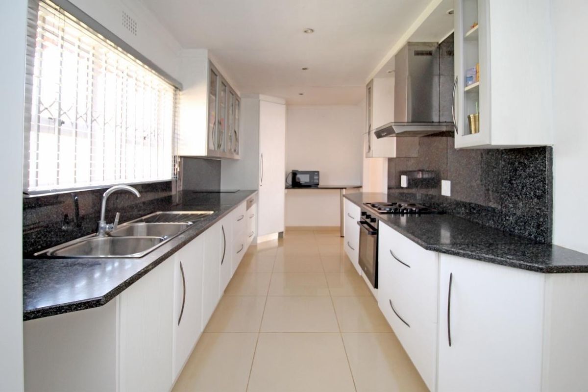 Modern galley-style kitchen featuring granite countertops, white cabinetry, stainless steel appliances, and tiled flooring with ample workspace.
