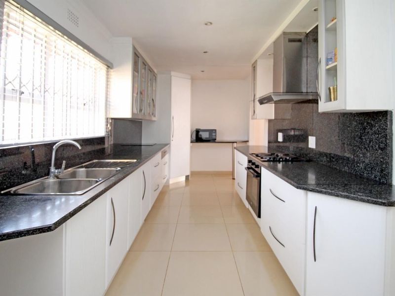 Modern galley-style kitchen featuring granite countertops, white cabinetry, stainless steel appliances, and tiled flooring with ample workspace.