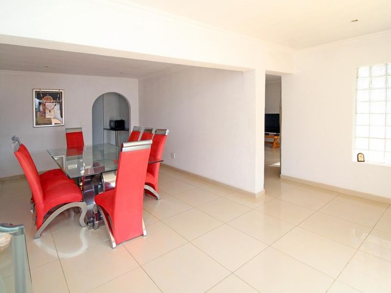 Open plan dining area featuring neutral tiled flooring, a glass block window, and an arched doorway leading to an adjacent space.
