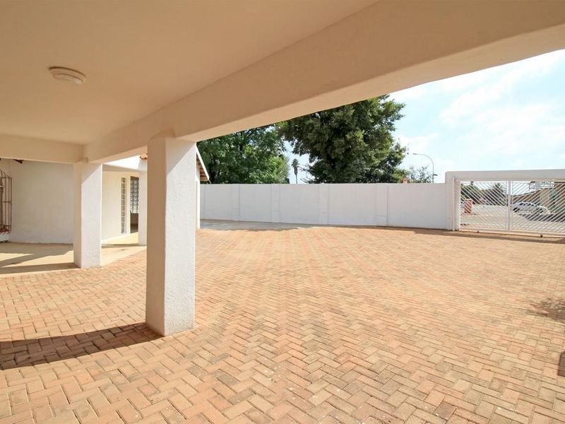 A spacious covered patio area overlooking a large brick-paved driveway and secure perimeter wall with a gated entrance.