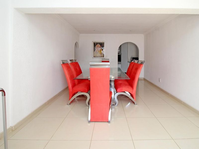 A bright dining room featuring neutral tiled flooring and arched architectural details leading to adjacent spaces.