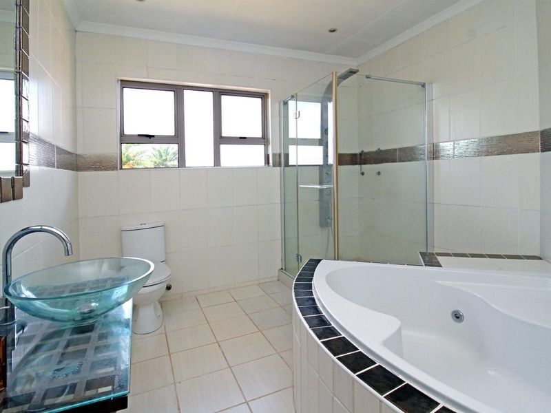 A bright, modern bathroom featuring a corner bathtub, a separate glass-enclosed shower, and a contemporary glass vessel sink with tiled finishes.