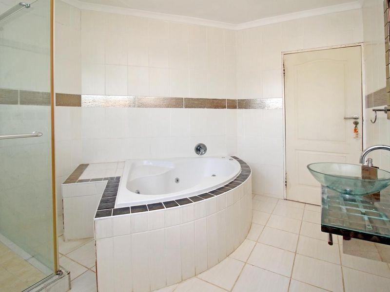 A spacious bathroom featuring a corner spa bath, a separate glass shower enclosure, and a modern glass vessel sink with wall-mounted fixtures.