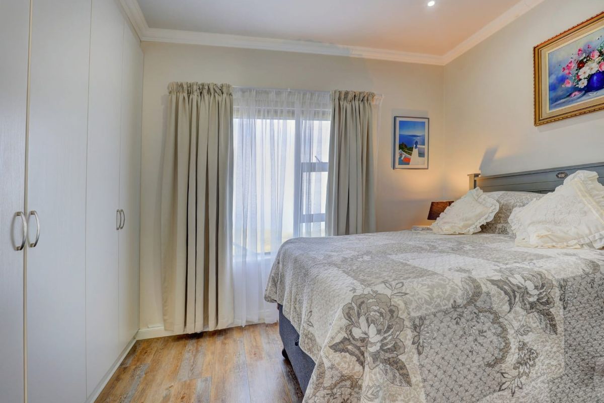 A well-maintained bedroom featuring built-in cupboards, modern laminate flooring, and neutral finishes, offering a comfortable and functional living space.