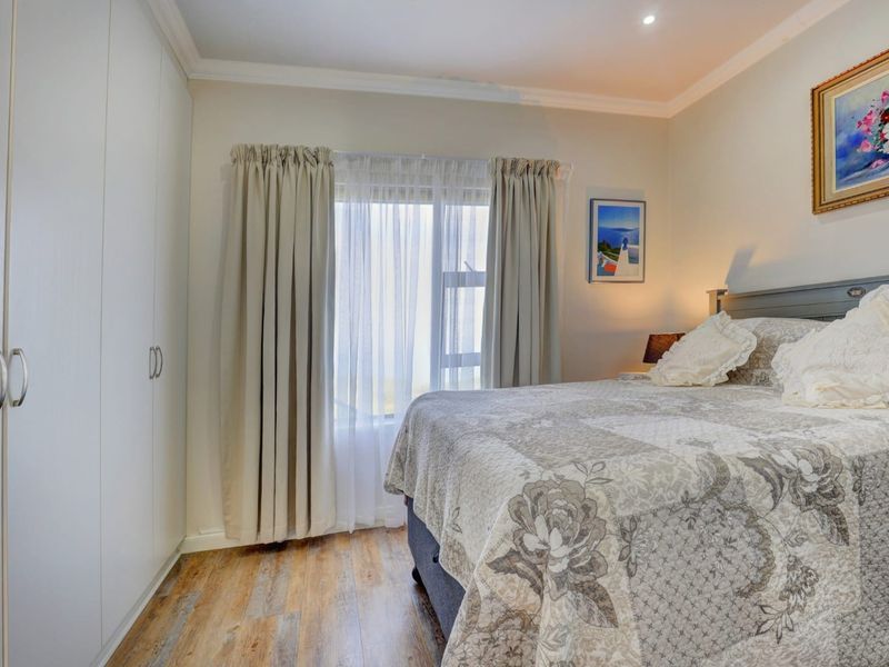 A well-maintained bedroom featuring built-in cupboards, modern laminate flooring, and neutral finishes, offering a comfortable and functional living space.