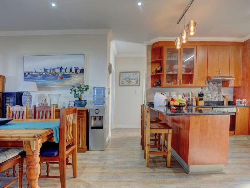 Open-plan living and dining area featuring a kitchen with granite countertops, wooden cabinetry, and modern lighting fixtures.